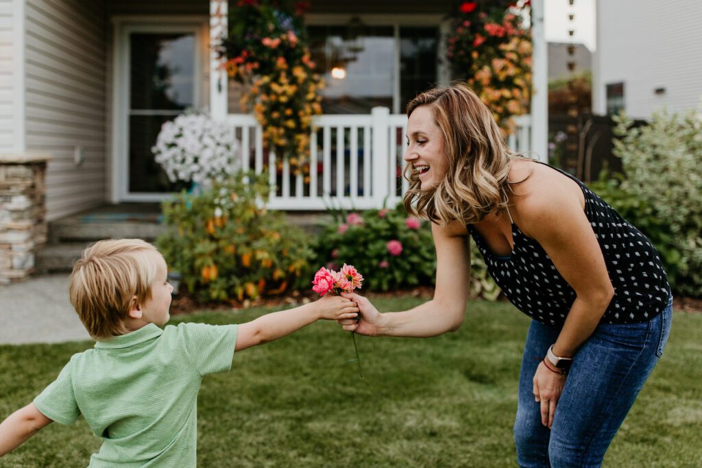 A mother receiving flowers from their young child in their front yard.