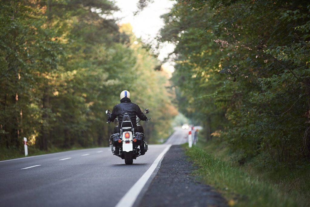 Back view of motorcyclist in black leather jacket riding down the road.