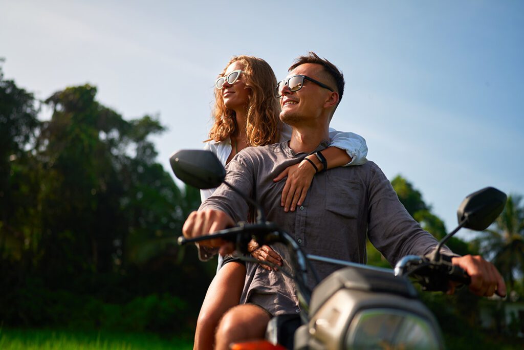 A young, smiling couple on a motorbike.