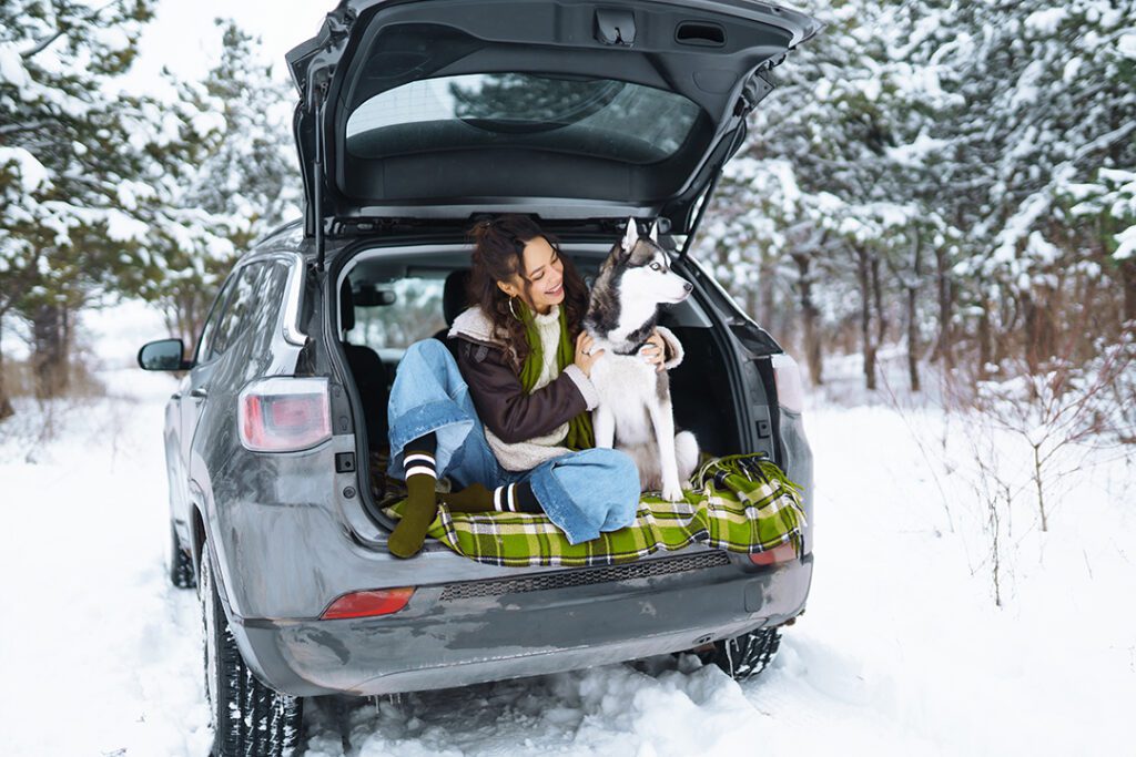 A young woman with her Husky in the car during a snowy day.
