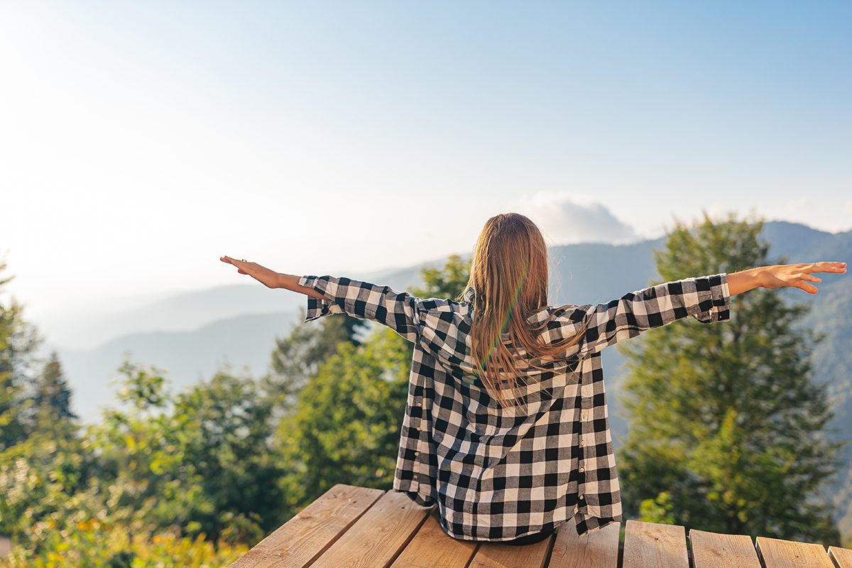 A happy young woman with her arms outstretched as if embracing the world around her.
