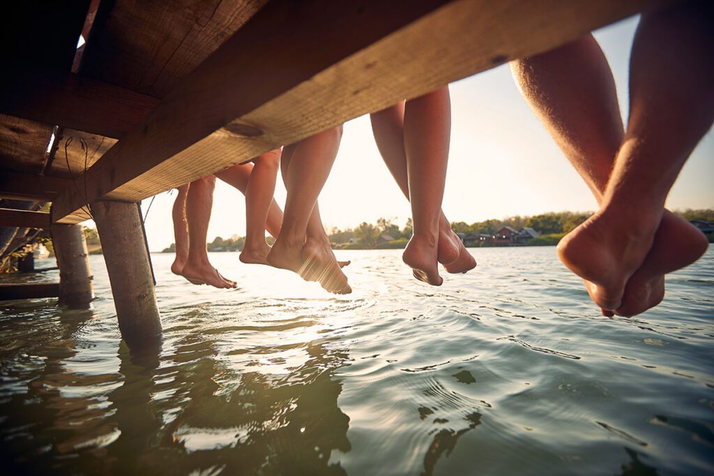 Friends sitting together on a dock with their feet dangling over the water.