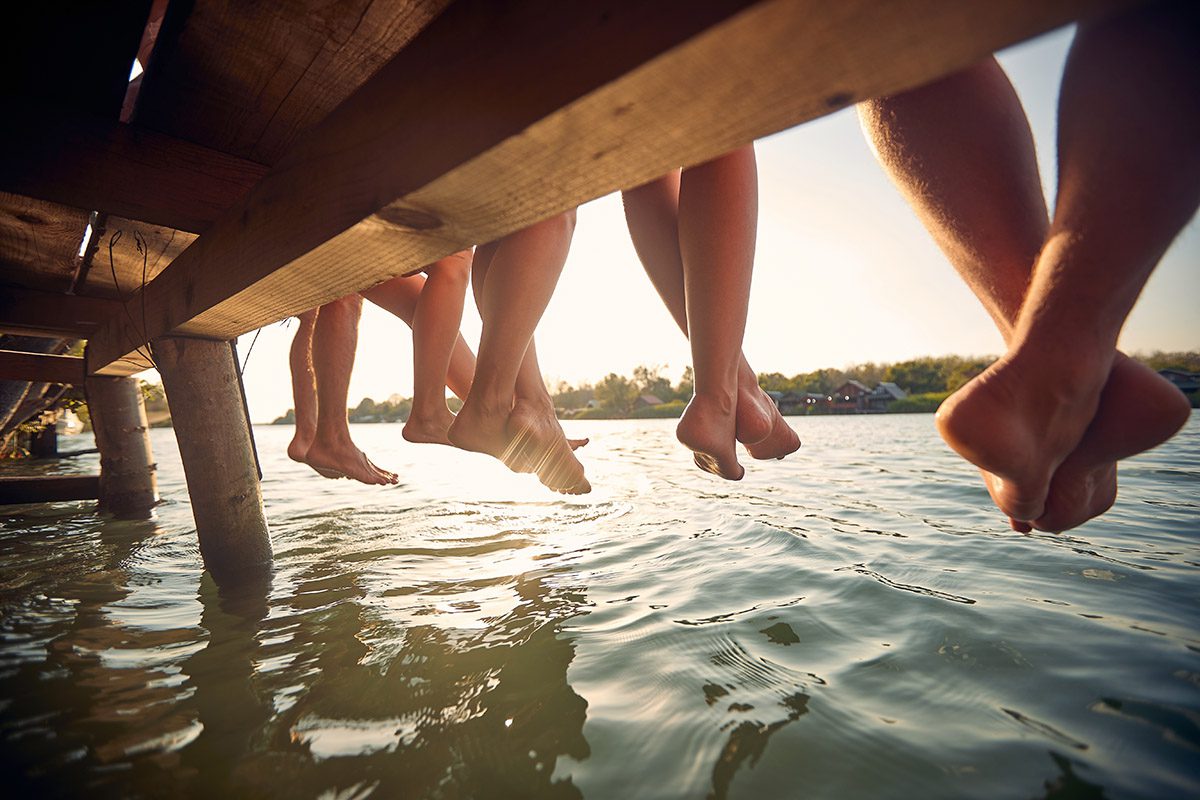 Friends sitting together on a dock with their feet dangling over the water.